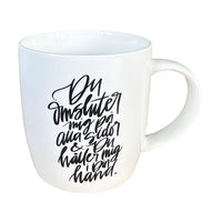En stilren, naturvit mugg med svart text ”Du omsluter mig på alla sidor & Du håller mig i Din hand.”