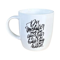 En stilren, naturvit mugg med svart text ”Du omsluter mig på alla sidor & Du håller mig i Din hand.”